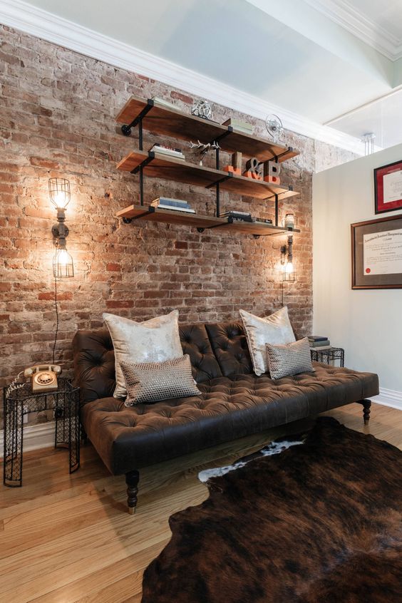 Sala de estar con pared de ladrillo visto estanterias de madera y metal sofa de cuero luminarias tipo fabrica y telefono vintage