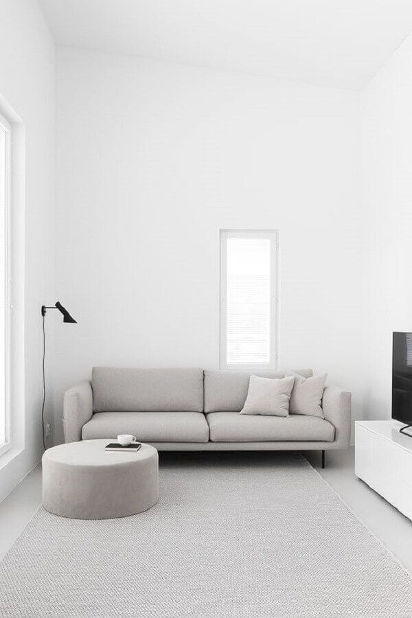 Salón de techo alto y sofá y alfombra de color gris, con toques en negro y paredes blancas.