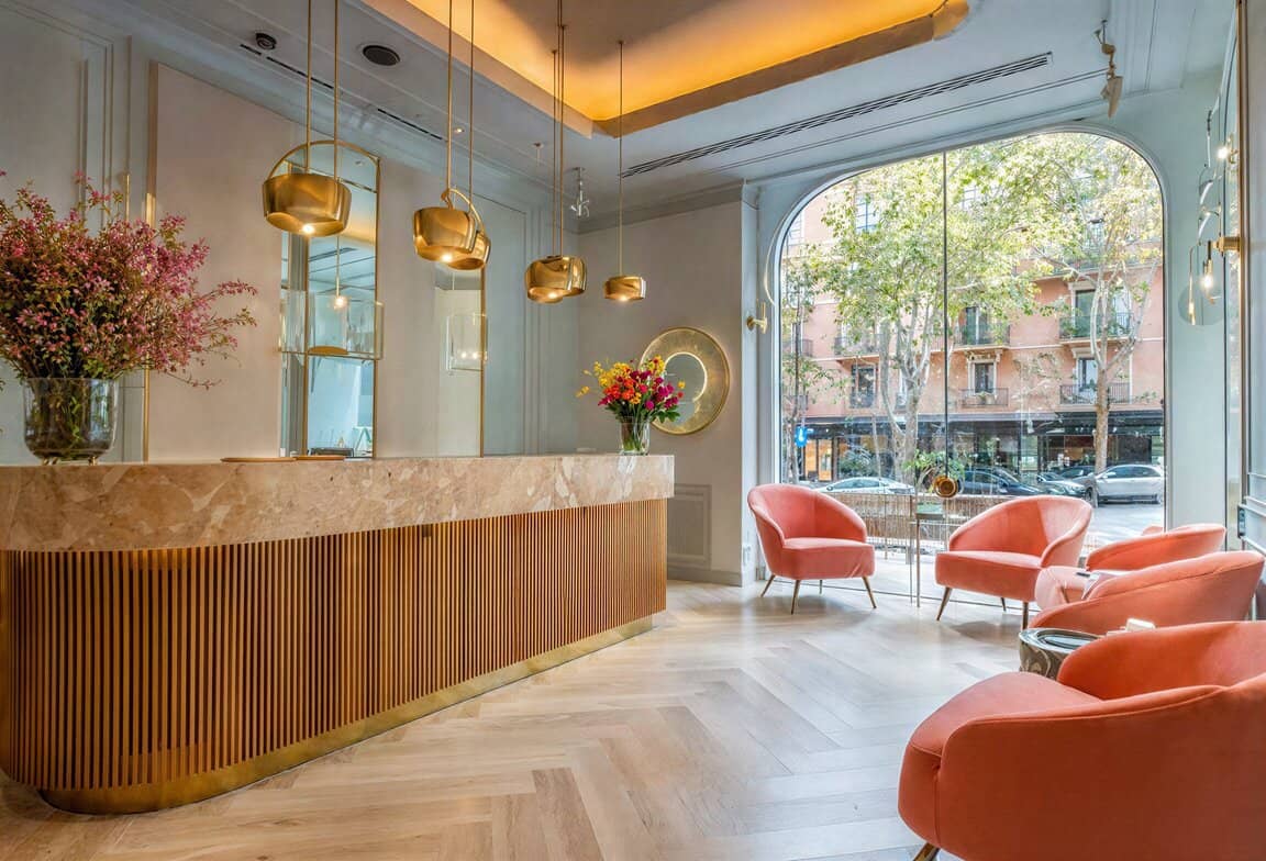 Proyecto de interiorismo de hotel boutique con mostrador de mármol y madera, lámparas doradas colgantes y sillones aterciopelados color rosa.